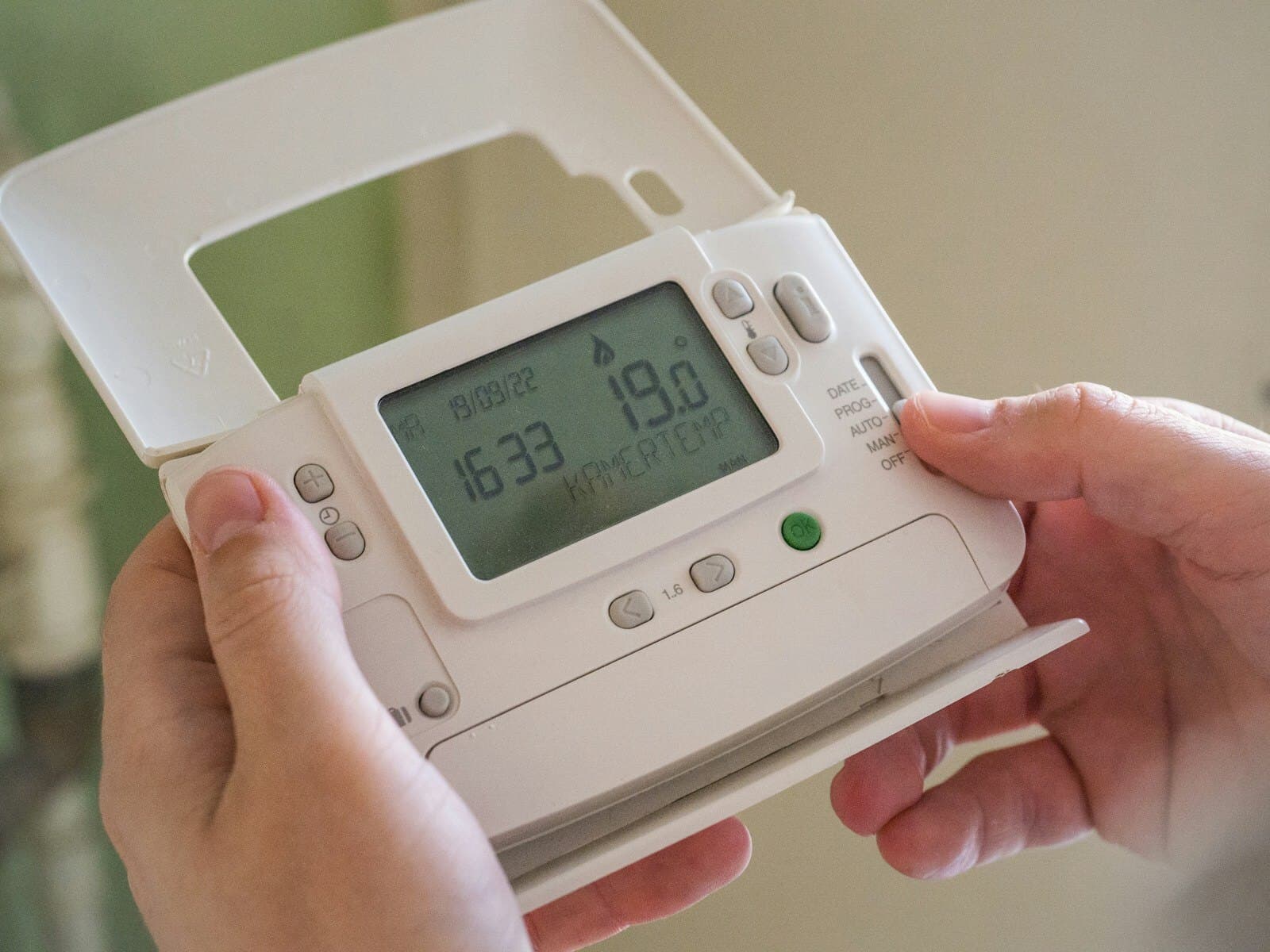 A hand adjusting a wall thermostat reading 19 degrees