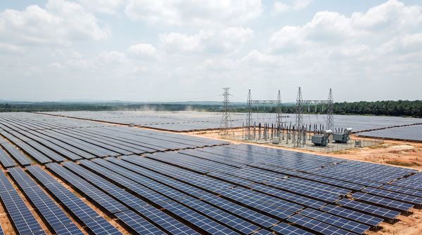 Aerial view of a large solar farm in Malaysia with rows of photovoltaic panels and a high-voltage transmission substation under a bright tropical sky