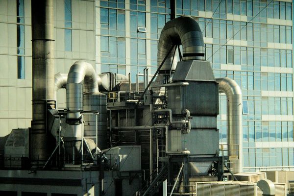 Building HVAC plant with air ducts and chilled-water pipework against an office tower