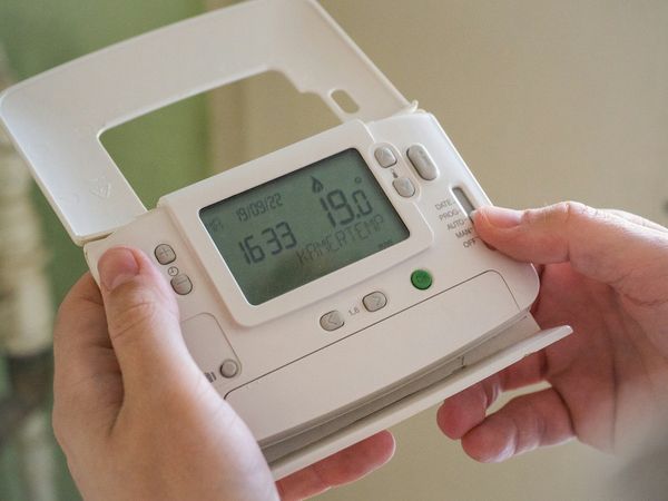 A hand adjusting a wall thermostat reading 19 degrees